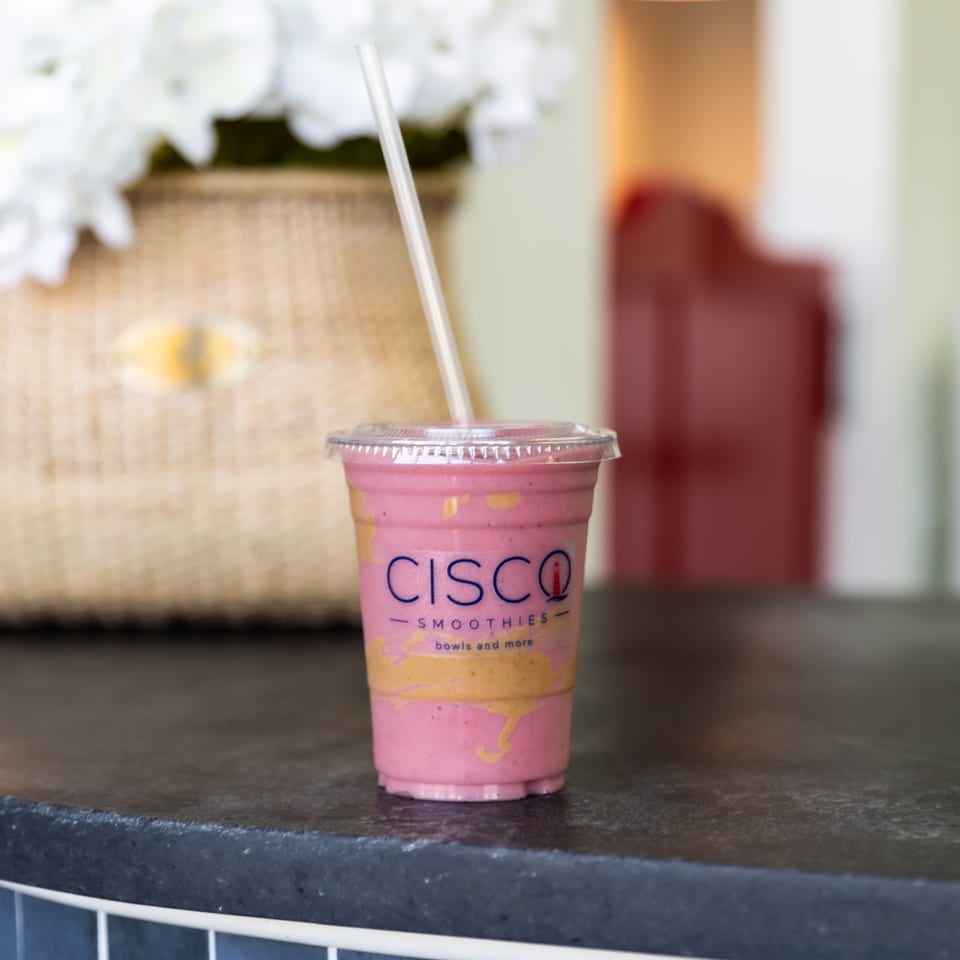 Pink smoothie in a Cisco Smoothies cup with a straw on the restaurant counter.