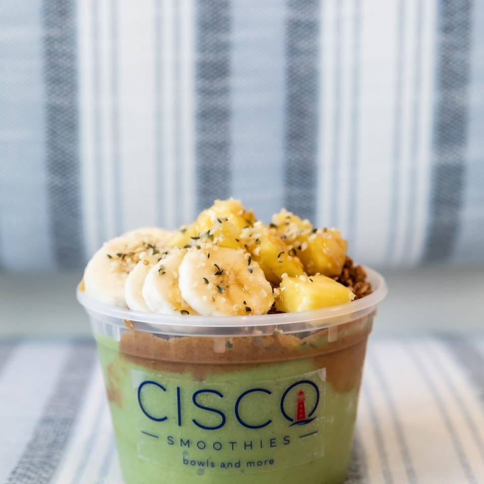 Green Cisco Smoothies bowl topped with banana slices, pineapple, granola, and seeds.